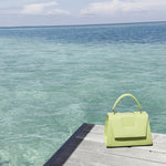 Discover the allure of this women's leather handbag in refreshing lemon hue. Featuring a structured cut, brand signature flap, brass accessories, and an adjustable strap, this handbag is the epitome of everyday elegance and style. Elevate your fashion with this chic accessory designed for the modern woman.